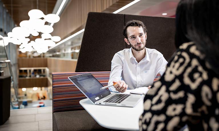 Two people sat at a desk facing each other and talking