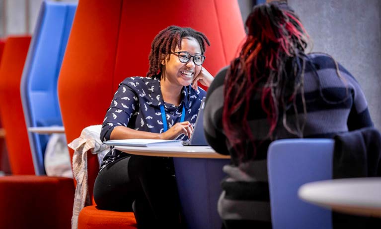 Member of staff sat at a desk talking to a student