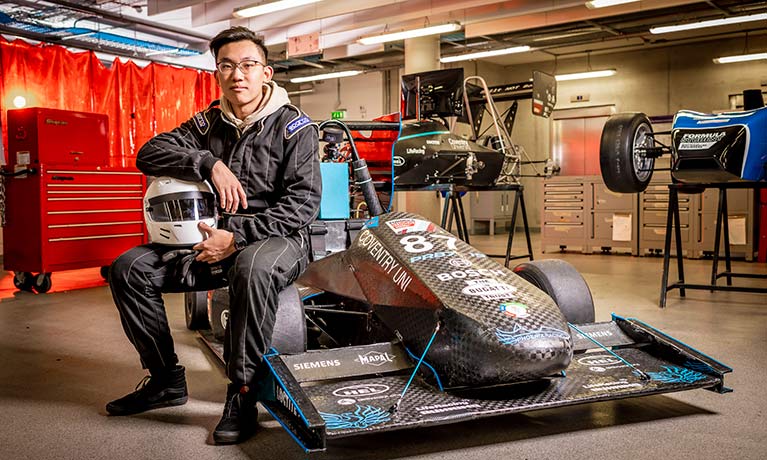 Young male student holding a helmet sitting on the wheel arch of a F1 motorcar