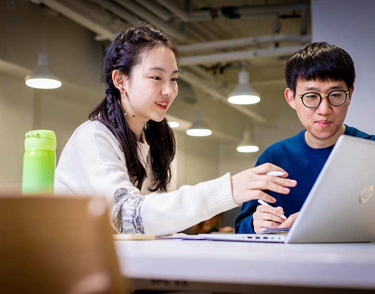 Two student sat next to each other looking at a laptop 