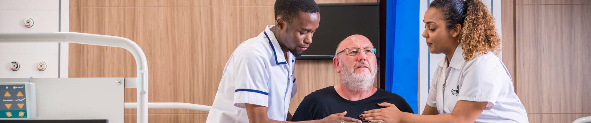 two student nurses assisting a patient with standing up, in a hospital setting