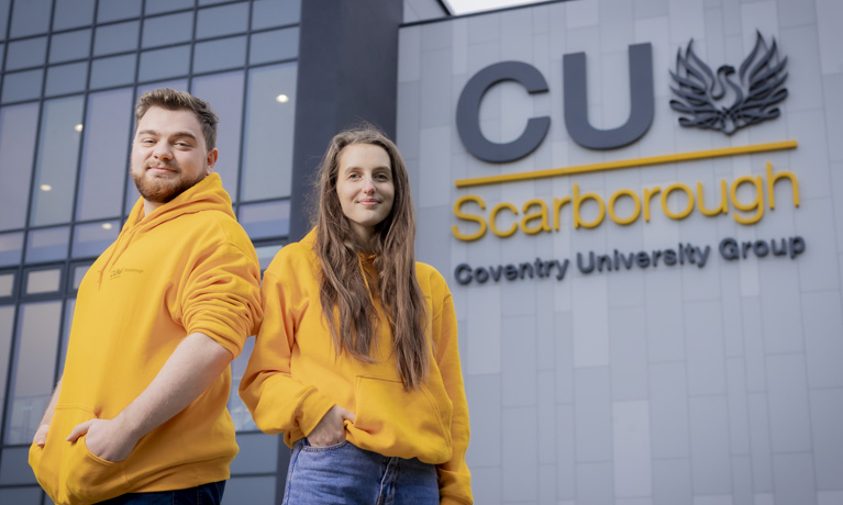 Two Scarborough students wearing bright yellow hoodies, stood outside the CUS building.