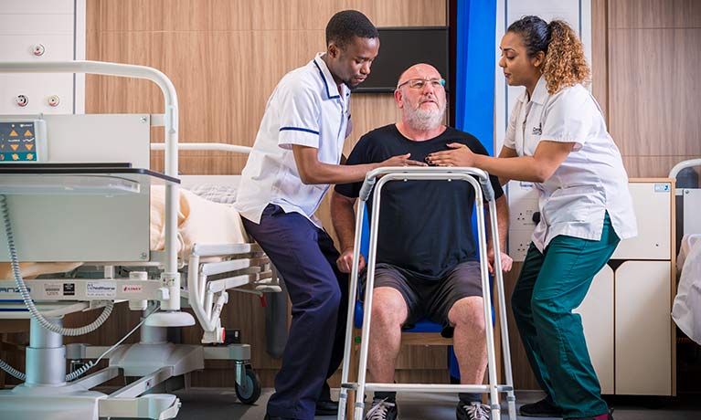 Two nursing students helping a patient to use a walking frame