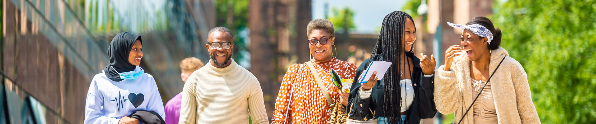 A family smiling as they walk past The Hub with the Cathedral ruins behind them.