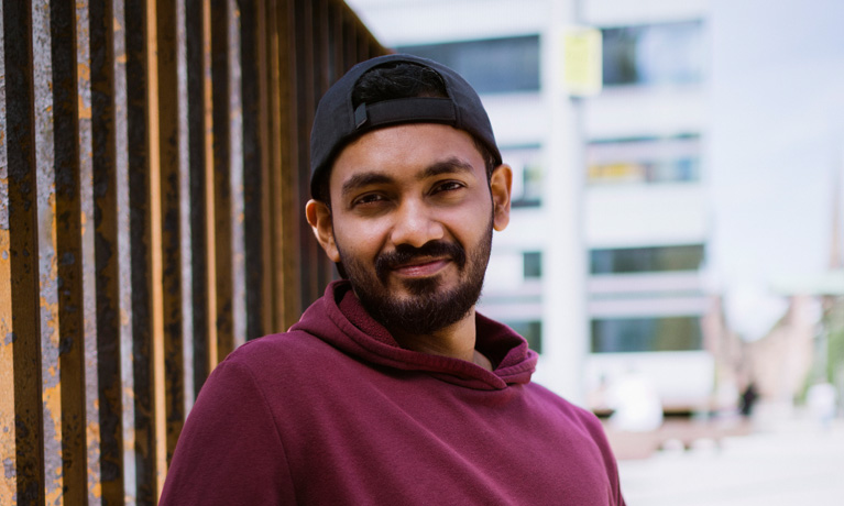 A make student leaning against a wall and smiling at the camera.