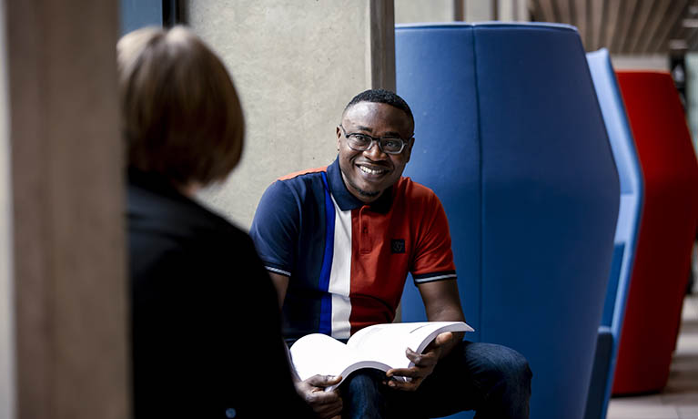 Male student in a study booth, smiling and holding a textbook.