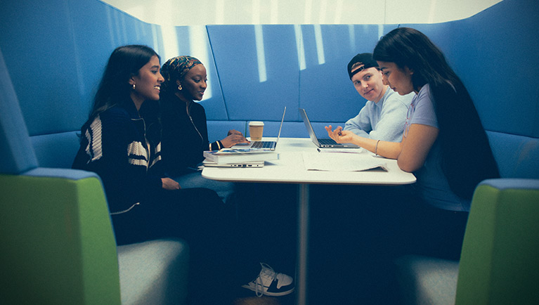 Students sat in a booth studying together and smiling