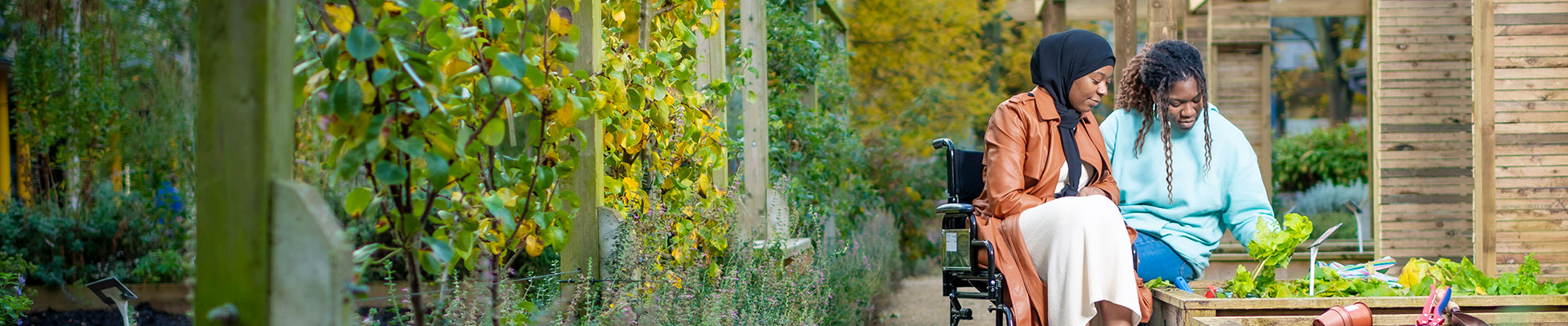 Female helping another female in a wheelchair look around a herb garden