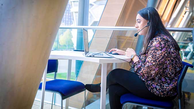 Female worker sat at a desk in front a window with a headset on a call