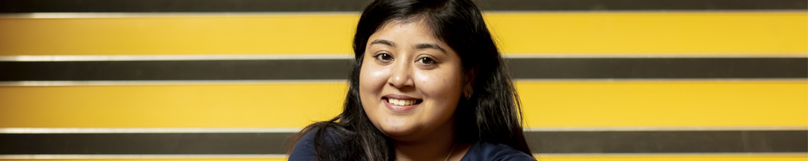 Student smiling against a yellow staircase background.