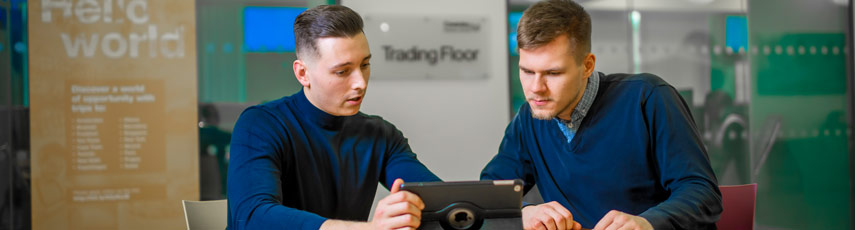 Two students sat at desk looking at iPad.