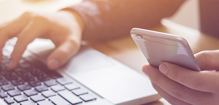 Close up of someone on laptop with mobile phone in other hand