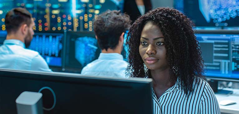 Lady in busy office looking at data computer monitor.