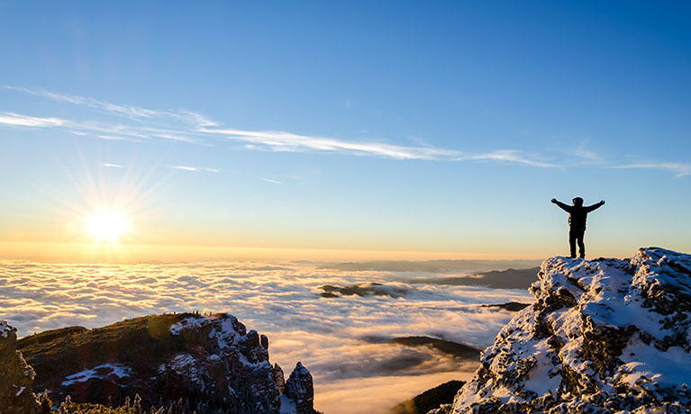 Hiker celebrating success on top of a mountain in a majestic sunrise