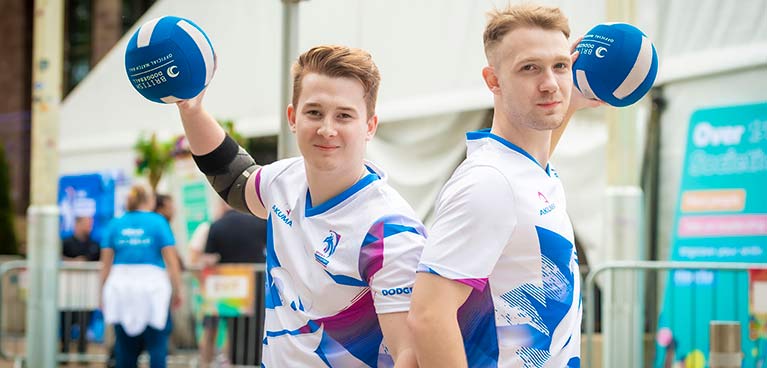 2 males adults in sports gear holding balls up 