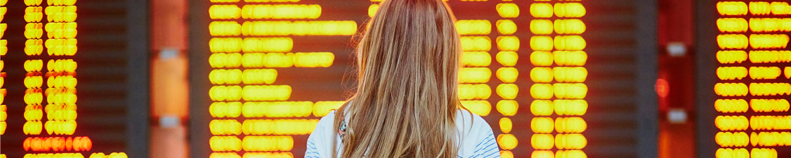 Back of girl looking at a flight information board in an airport.