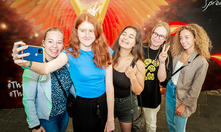 A group of students taking selfies in front of phoenix street art.