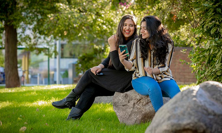 Two female students talking outside in the sunshine