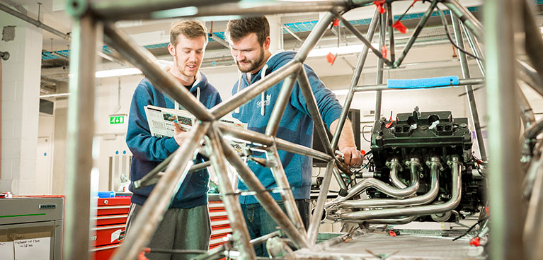 Motorsport students welding in a laboratory while reading through documentation