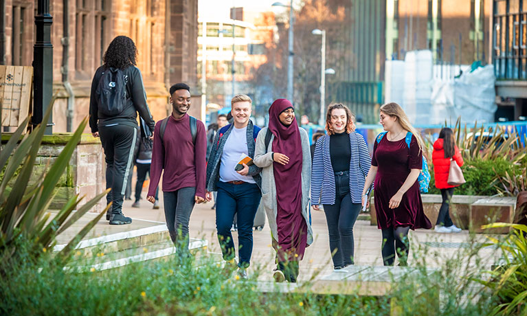 Five students walking through Coventry talking and smiling