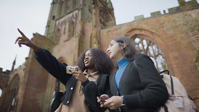 Two female students stood in the cathedral ruins on a cloudy day