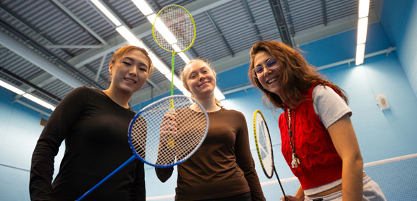 three students smiling with badminton rackets