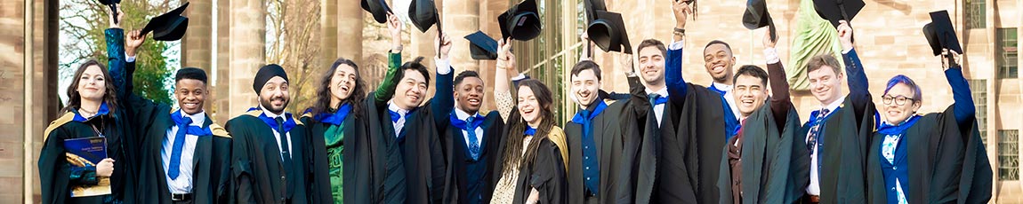 Group of students wearing graduation gowns lined in front of an old historic building