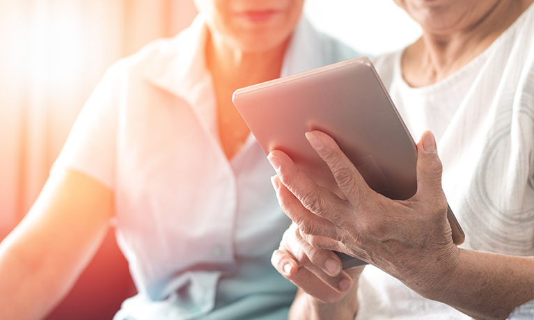 A lady showing an elderly person how to use a smart tablet