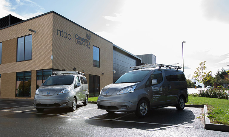 Two electric vans parked outside of a building