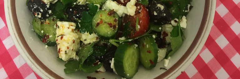 Top down view of a bowl of salad on red checkered table cloth.