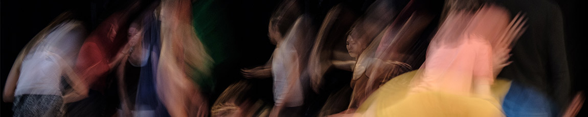 A woman wearing a white mask dances in a dark building