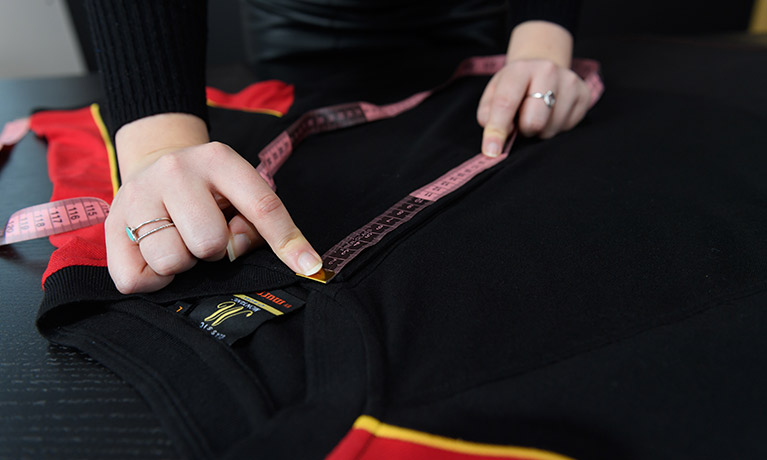 Hands use a tape measure to measure a black t-shirt