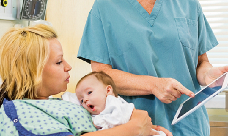 Newborn baby held by its mother next to healthcare professional