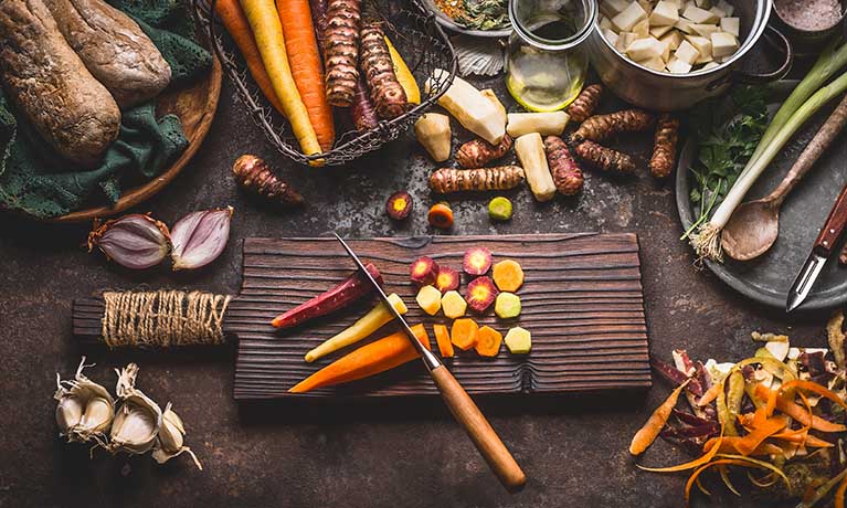 Carrots being chopped on a board with other veg surrounding it.