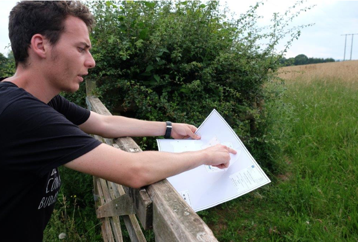 Man standing with map, leaning on fence