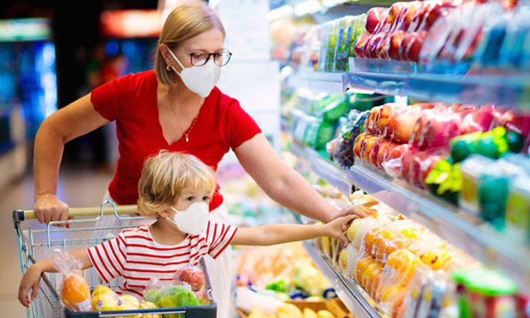 A lady in a supermarket wearing a Covid mask with a child in the trolley