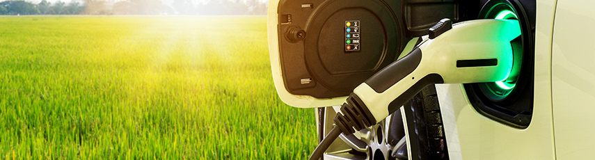 EV car plugged in to charge with a field backdrop