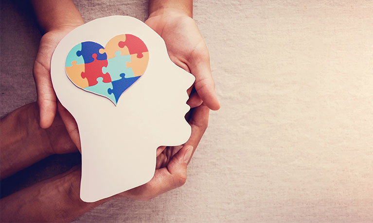 a cardboard silhouette of a head with coloured jigsaw pieces forming a heart shape on it.