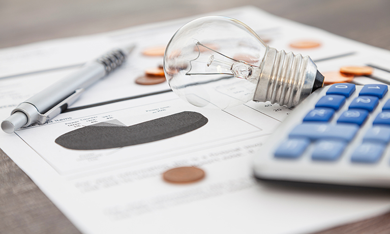 A light bulb, a pen, a calculator and some copper euro cent coins lie on top of an electricity bill