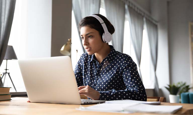 a woman sitting at a laptop wearing headphones