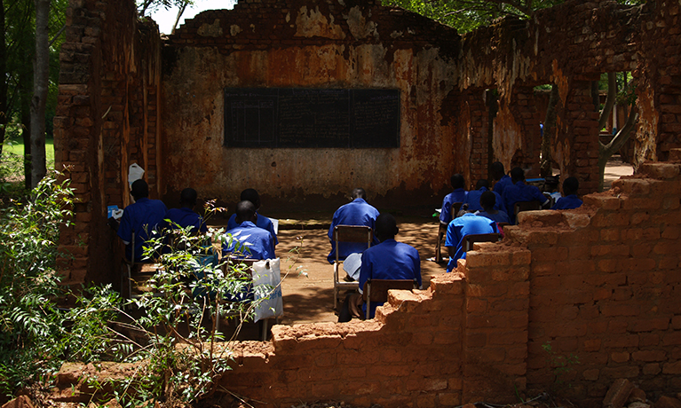 People working at chairs in a bombed out school in Sudan