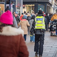 Pedestrians on a busy UK pavement with a police officer in a high-vis vest