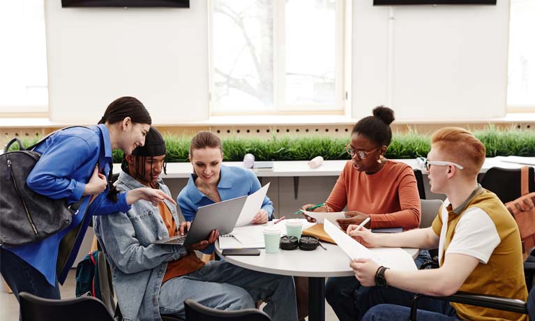 Five students sat at table working with notes and laptop