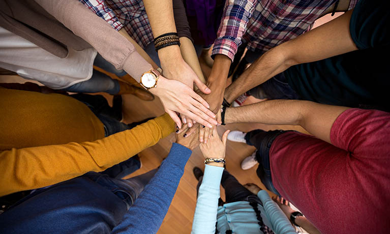 A diverse set of hands one on top of the other in a circle