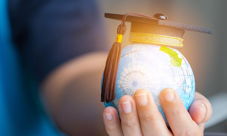 A hand holding a globe topped with a graduation cap.