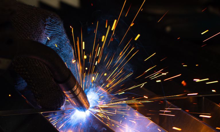 close up of machinery in a dark setting with sparks flying off where the machine meets a metal coil 