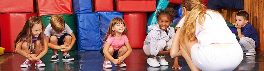 Children crouching down in a PE lesson with their teacher