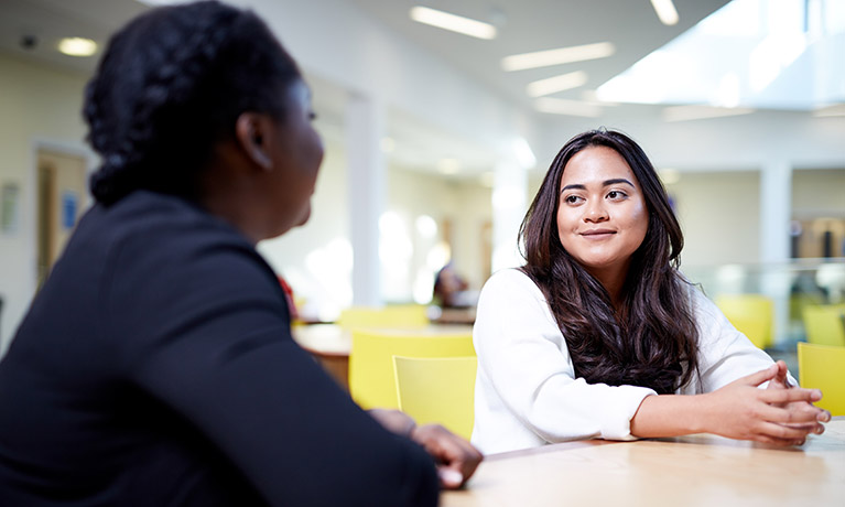 Two female students sat inside the Jaguar building talking