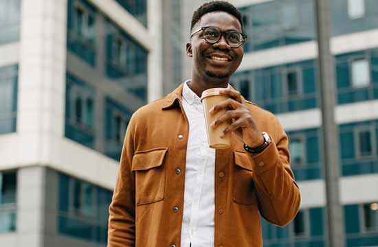 Smiling man holding a cup of coffee outside a tall building