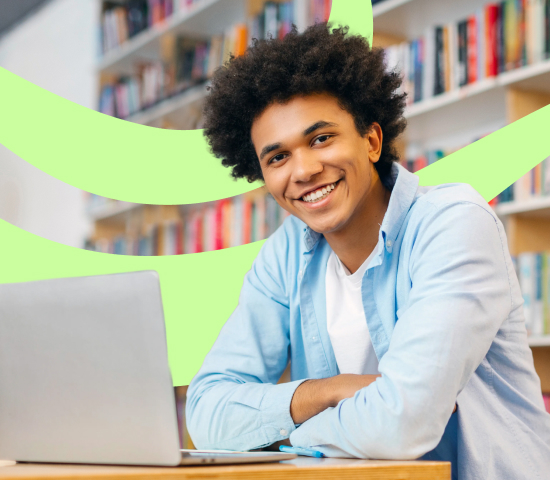 Smiling young man sitting in a library with an open laptop in front of him